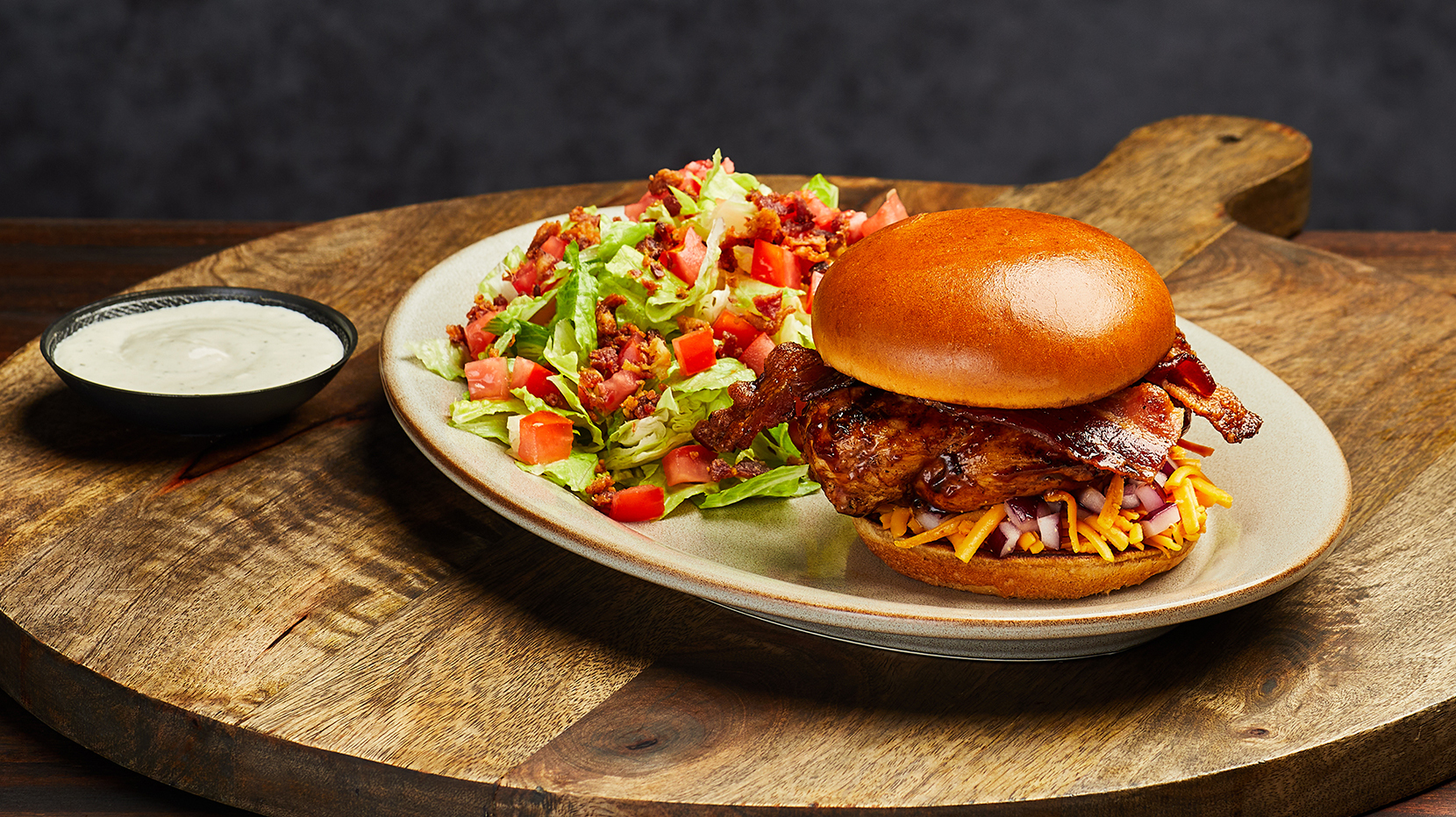 A Firebirds Smokehouse Chicken sandwich with a side of ranch dipping sauce and salad.