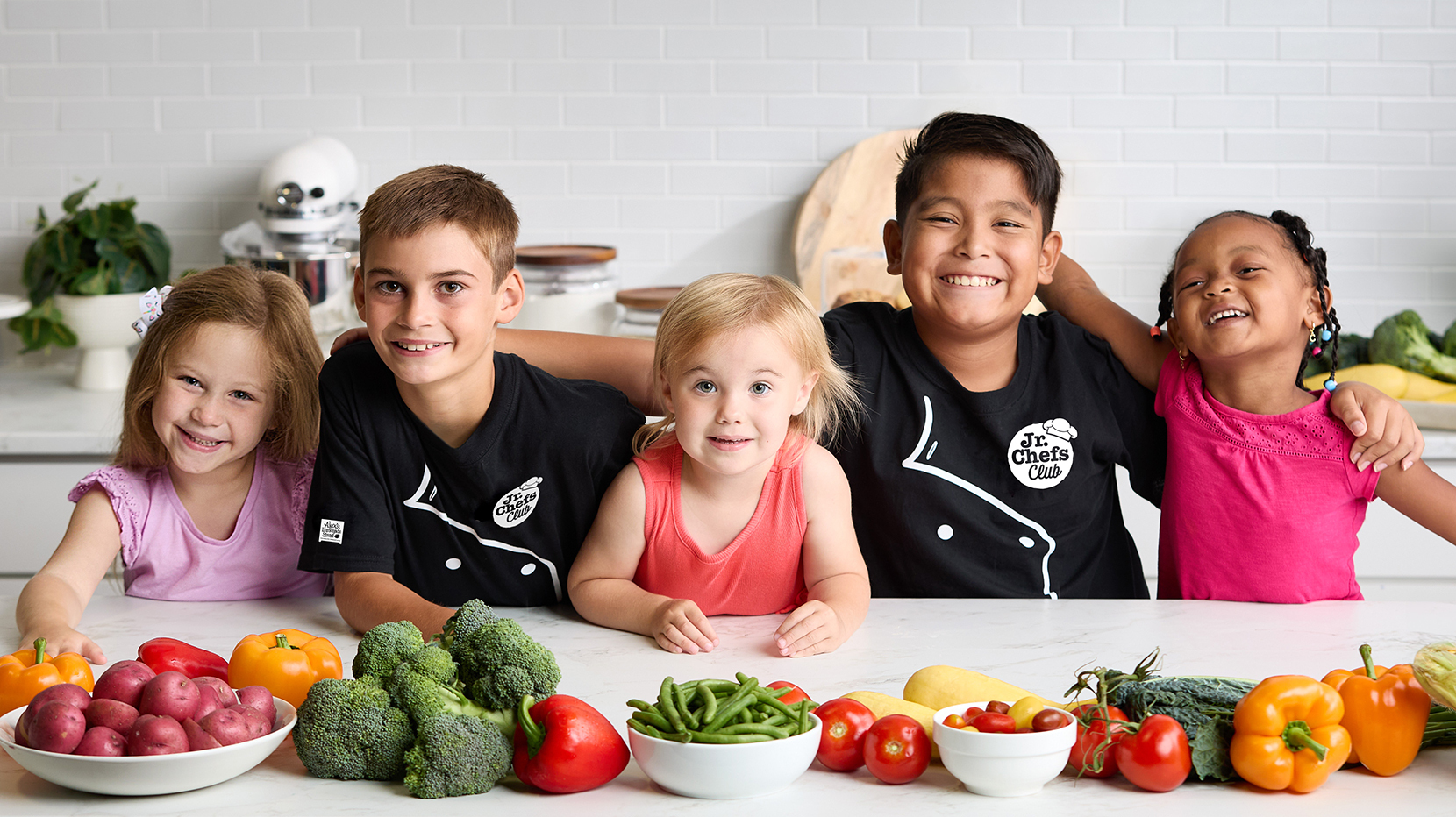 Five children at a counter with vegetables on it